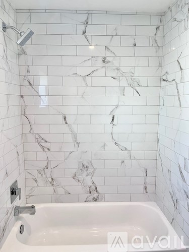 A white marble tiled bathroom with a white bathtub and a shower head.