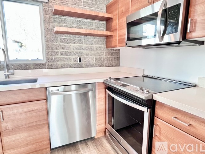 A kitchen with a stainless steel dishwasher and oven, wooden cabinets, and a brick wall.