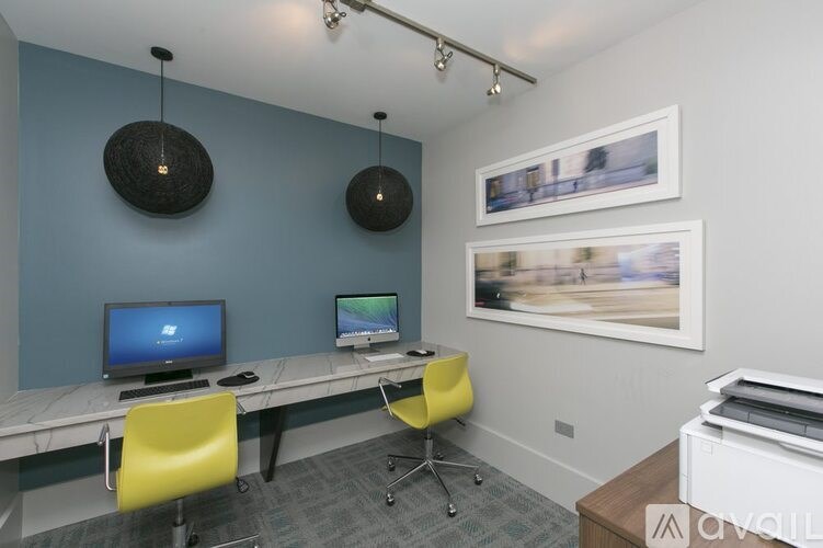 A room with a desk, two computers, and chairs.