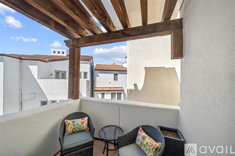 A balcony with a chair, table and cushions overlooks a town.