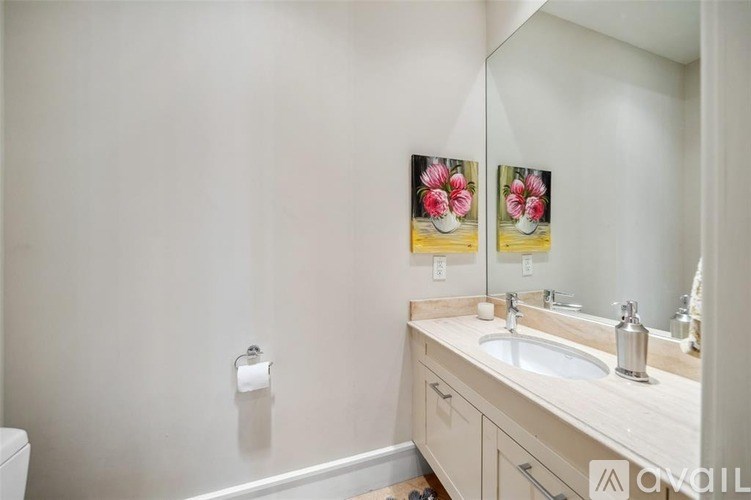 A bathroom with a toilet, sink, mirror, and a picture of flowers on the wall.