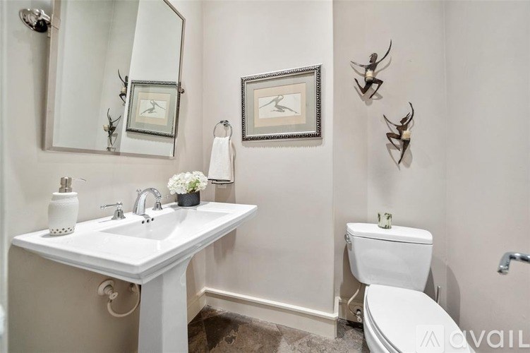 A white sink and toilet in a bathroom with a mirror and wall art.