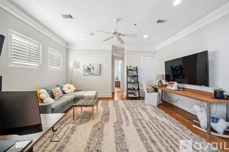 A living room with a grey couch, a black television, a wooden coffee table, a rug, and a ceiling fan.