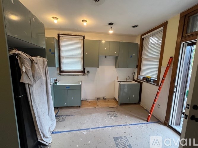 A room under renovation with a window, cabinets, and a ladder.