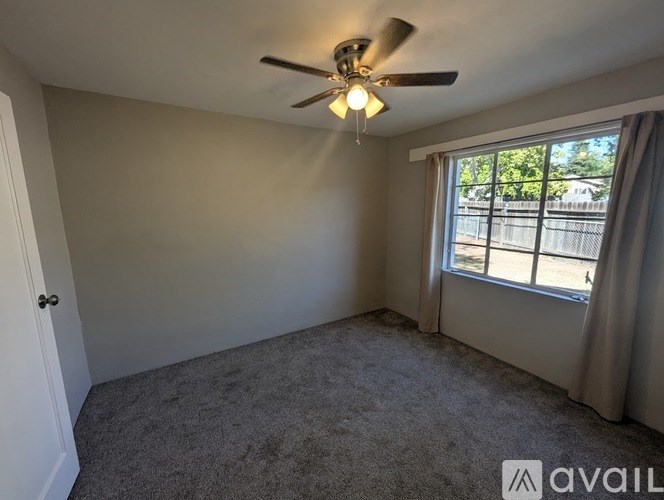 A room with a ceiling fan and a window with curtains.
