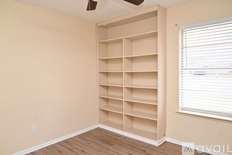 A room with a large open shelving unit and a window with blinds.