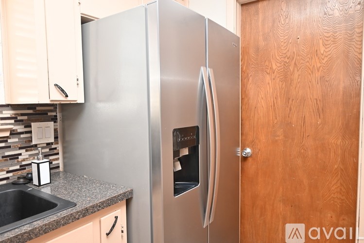 A stainless steel refrigerator is in a kitchen with a sink and wooden door.