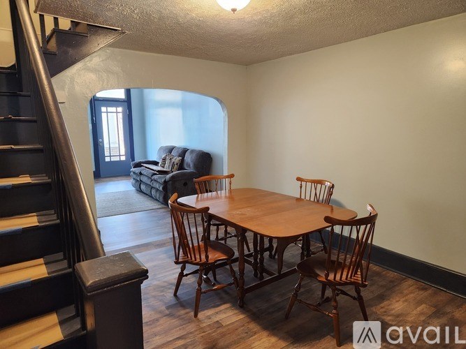 A wooden dining table with chairs is in a room with a staircase.