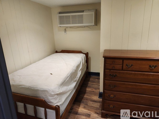 A bedroom with a bed, dresser, and air conditioner.