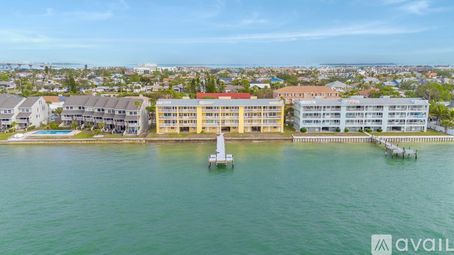 A large building with a red roof is surrounded by water and has a white boat in front of it.