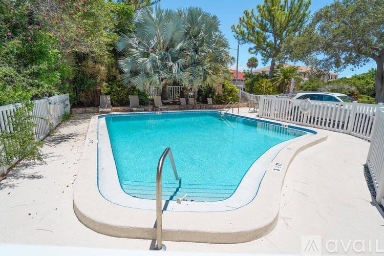 A small residential pool surrounded by a white fence and trees.