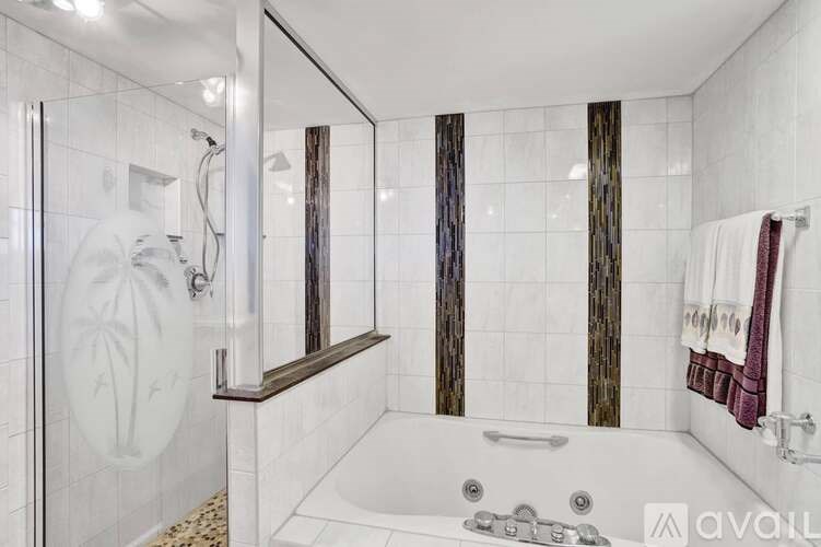 A white tiled bathroom with a glass shower door and a white bathtub.