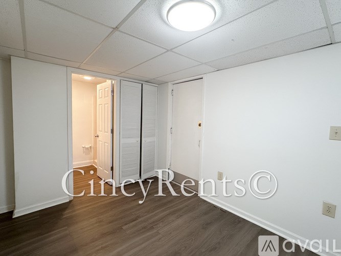A room with white walls and wooden flooring, with a doorway leading to another room.