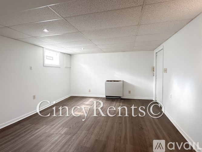 A room with wooden floors and white walls, with a window on the left wall and a door on the right wall.