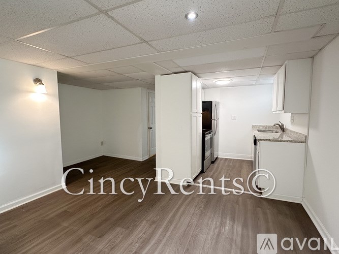 A room with wooden flooring and white walls, with a kitchenette in the corner.