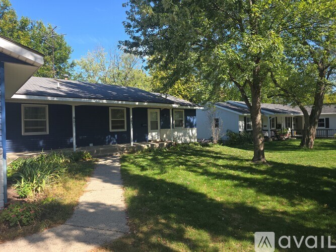 A house with a blue exterior is surrounded by greenery and has a clear blue sky above.
