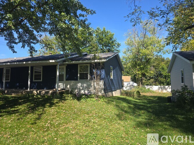 A house with a blue roof and white walls is surrounded by greenery.