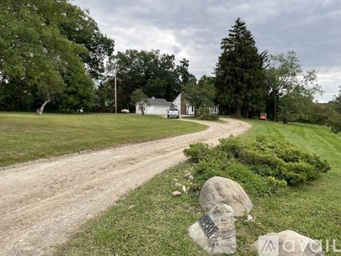 A dirt road leads to a white house in a grassy field.