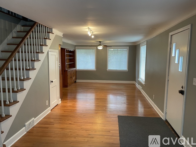 A spacious room with wooden floors and a staircase on the left side.