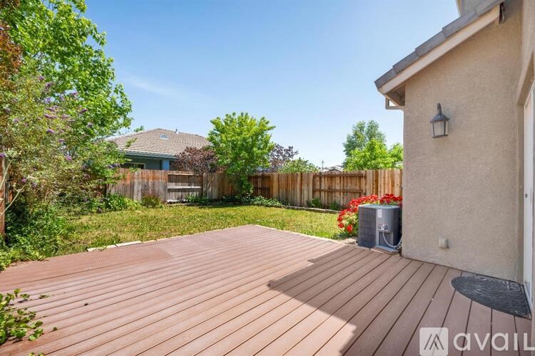 A wooden deck leads to a house with a fence and greenery in the background.