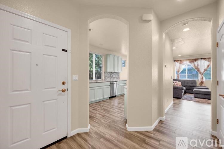 A white door is open to a hallway with a kitchen in the background.
