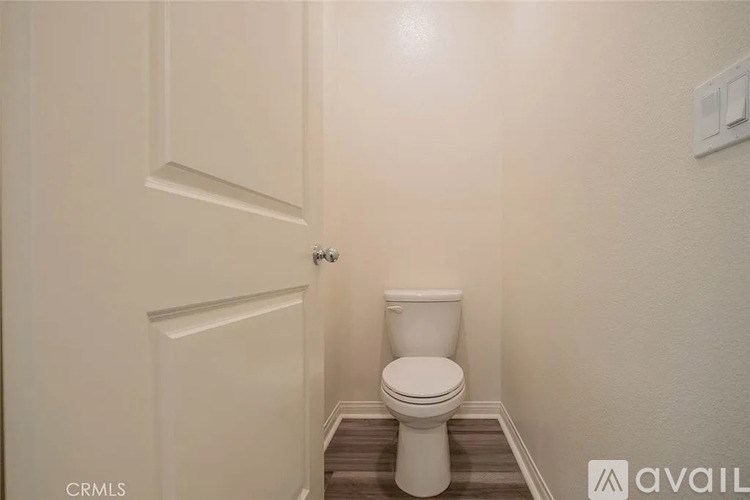 A white toilet in a small bathroom with a door and a light switch.