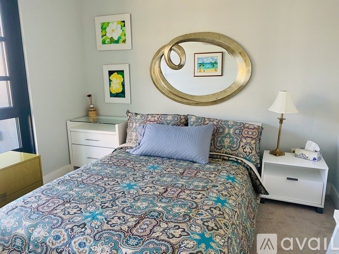 A bedroom with a patterned bedspread and a round mirror above it.