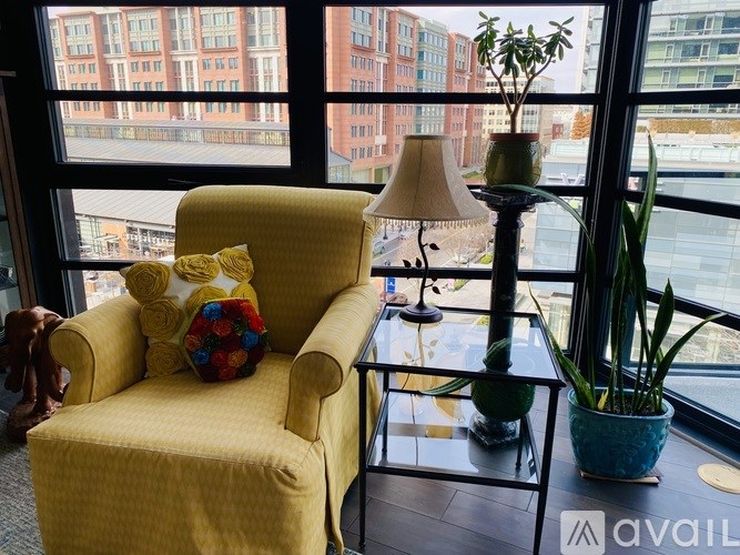 A yellow chair with a cushion and a lamp on a table in front of a window.
