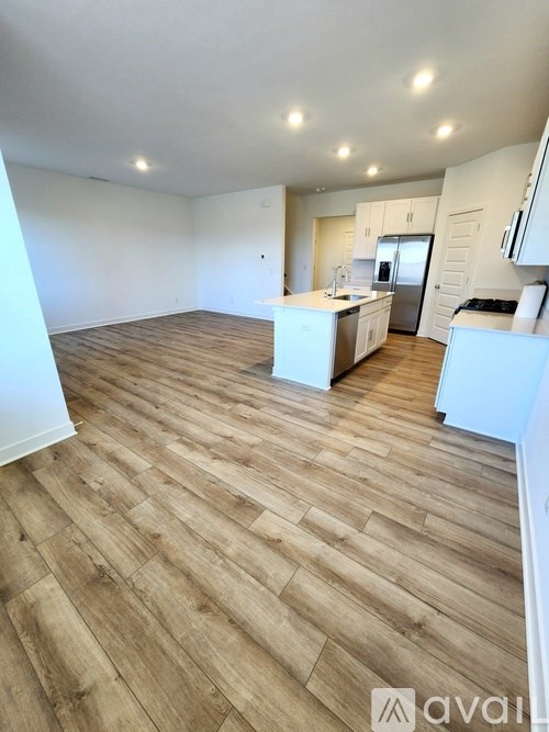 A spacious room with wooden flooring and a kitchen area in the background.