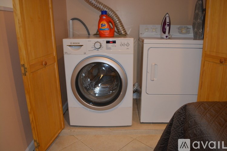 A white washing machine with a hose coming out of it and a bottle of detergent on top.