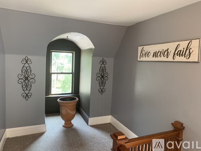 A room with a wall decoration that says "love never fails" and a window with a view of trees.