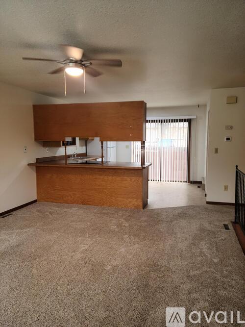 A living room with a ceiling fan and a kitchen area in the background.