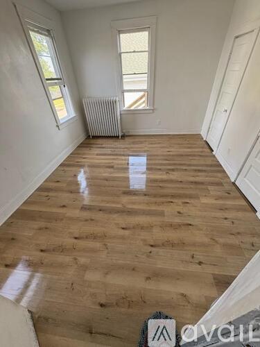 A room with wooden flooring and white walls, with a window and a radiator.