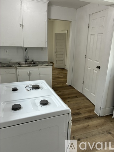 A white stove top oven with four burners is in a kitchen with white cabinets and a white door.