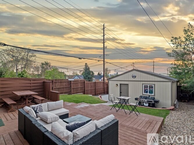 A backyard with a wooden deck, a hot tub, and a small house.