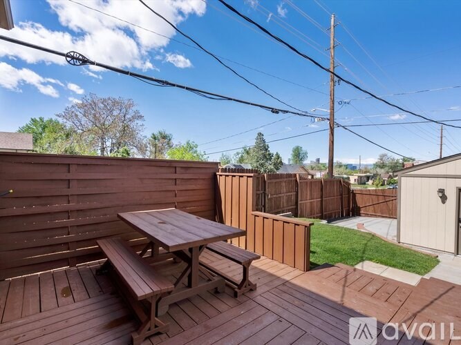 A wooden table and bench on a deck with a fence and trees in the background.