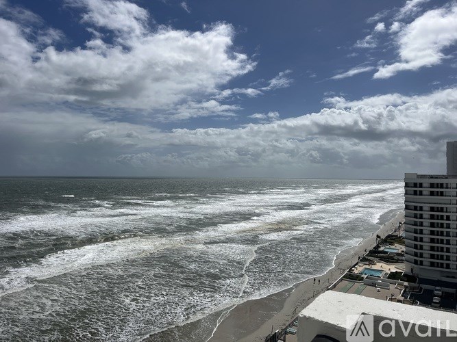 A view of a beach with waves crashing onto the shore and a hotel in the background.