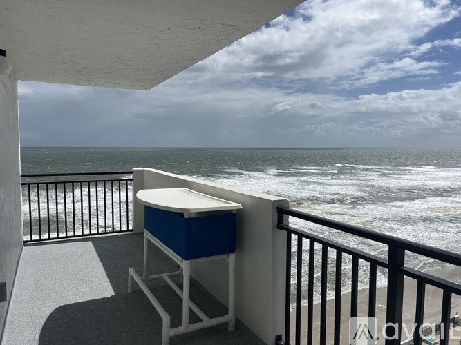 A blue and white cooler sits on a balcony overlooking the ocean.