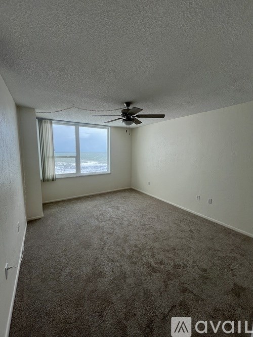A room with a ceiling fan and a window overlooking the beach.