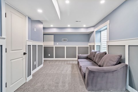 A spacious living room with a grey sofa and a grey carpet.