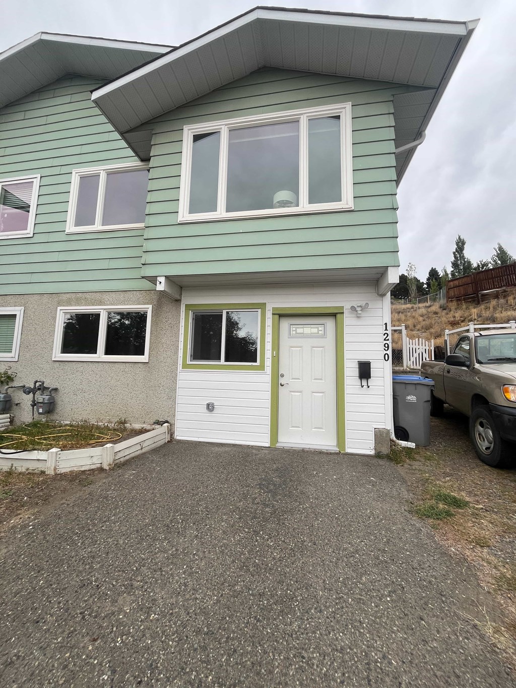 A green house with a white door and a truck parked in front.