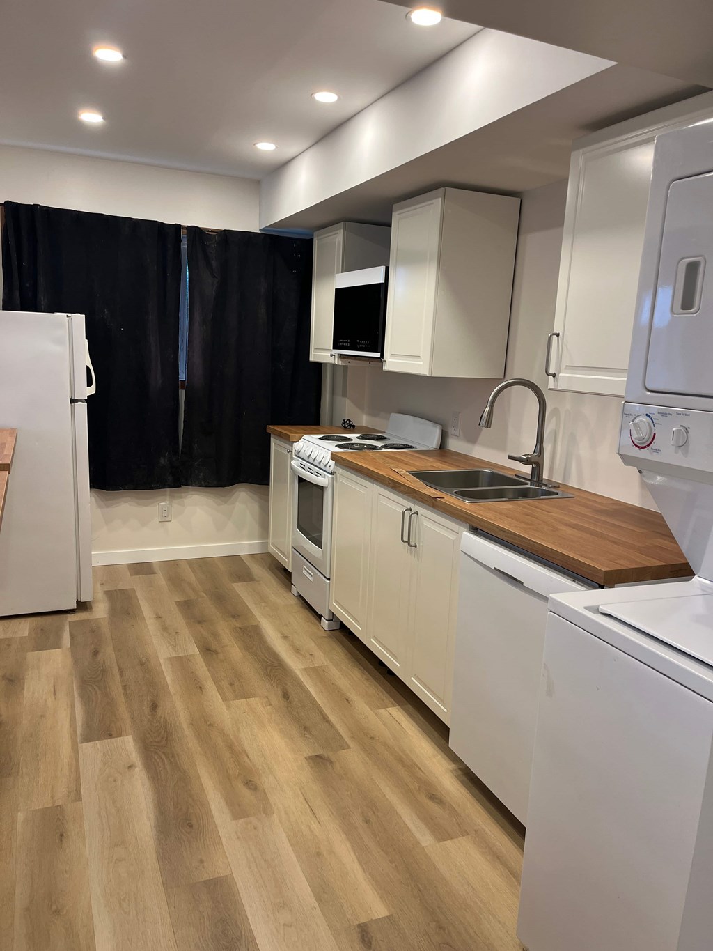 A kitchen with white appliances and wooden floors.