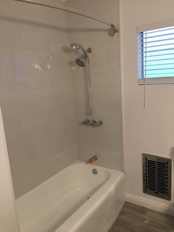 A white bathtub with a shower head and a window with blinds.