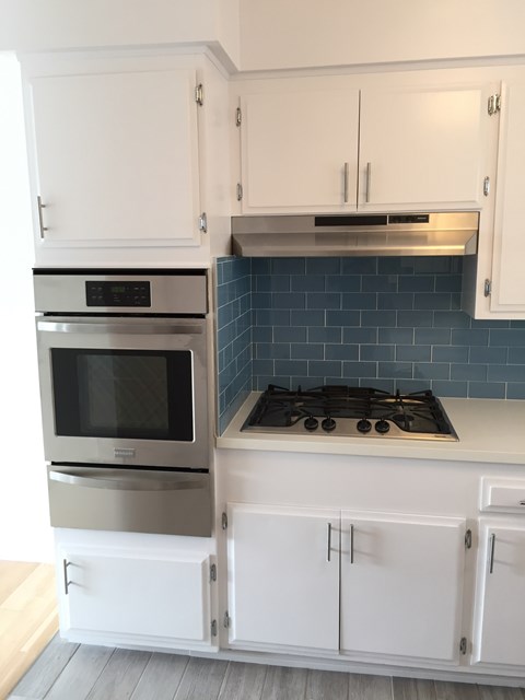 A kitchen with white cabinets and a stove top oven.