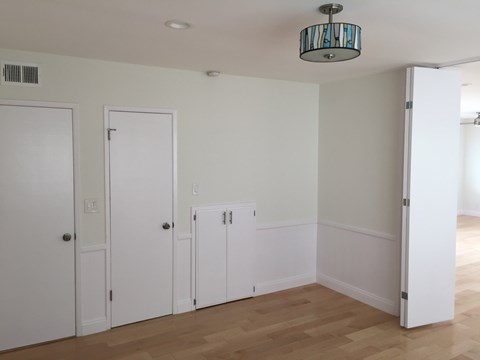 A room with white walls and wooden floors with four doors.