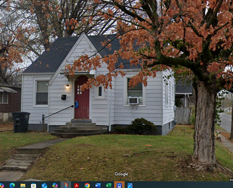 A small white house with a red door and a tree with orange leaves in front.