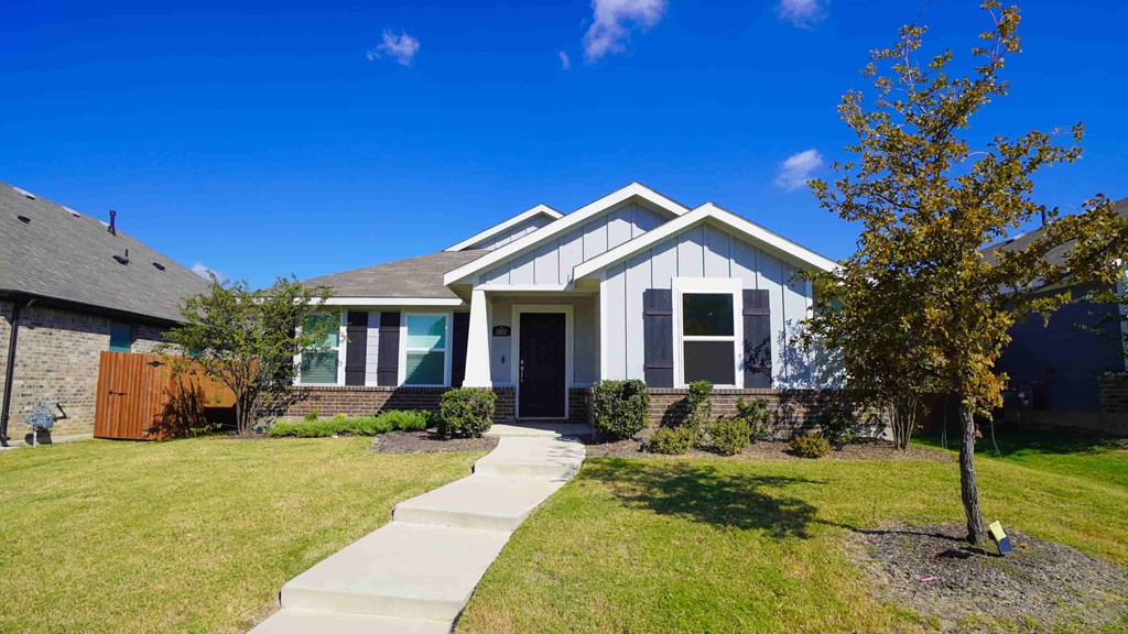A house with a grey roof and white walls with a small tree in front.