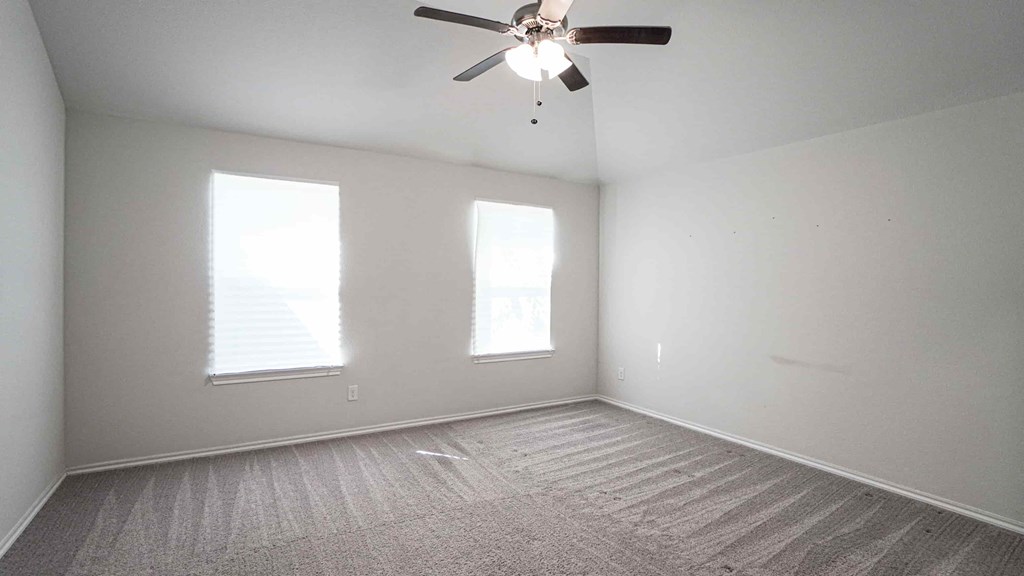 A room with a ceiling fan and two windows.