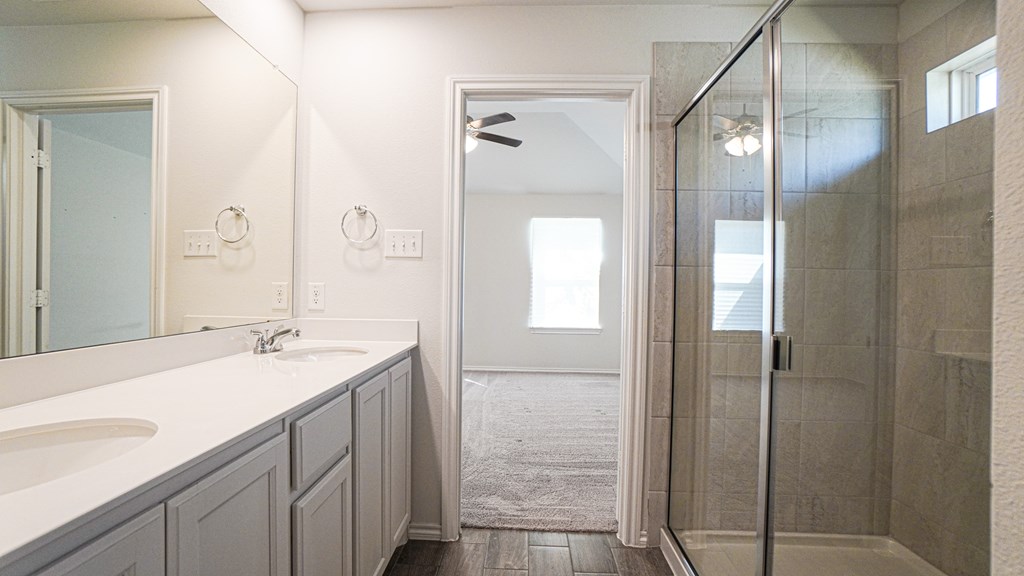 A bathroom with a walk in shower and double sinks.