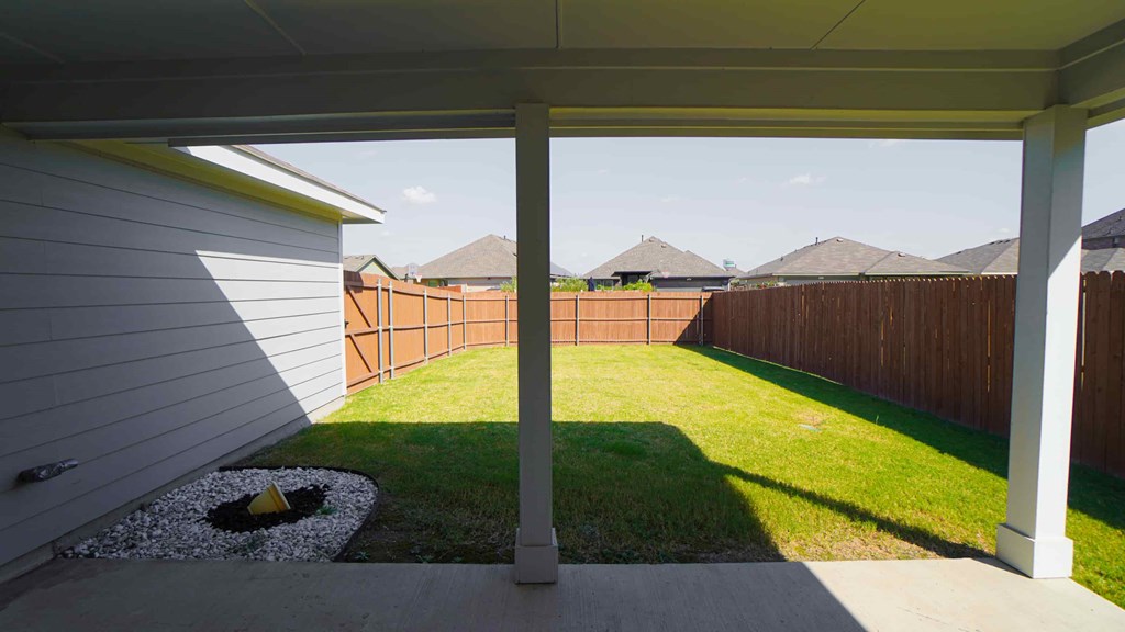 A view from a covered patio looking out to a backyard with a fence.